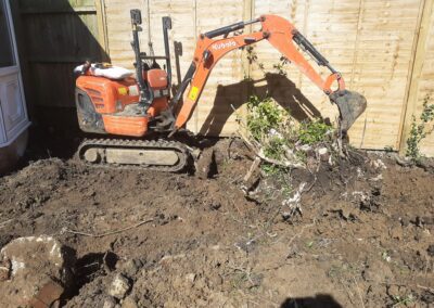 A garden and tree stump that's being dug out using a mini digger and driver hire service