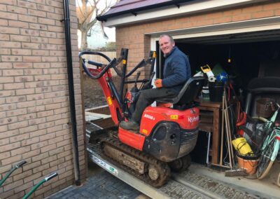 The mini digger and driver going through a narrow garden gate.